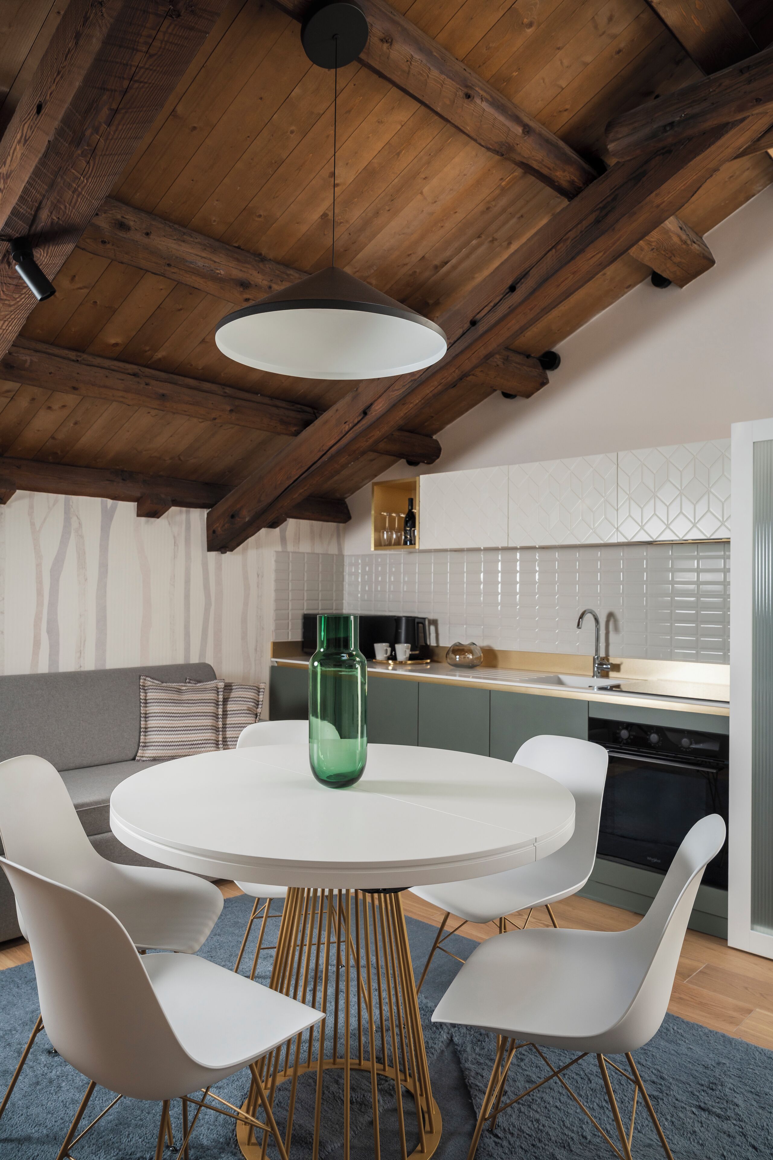 A modern kitchen with a round dining table, white chairs, and a hanging light fixture.