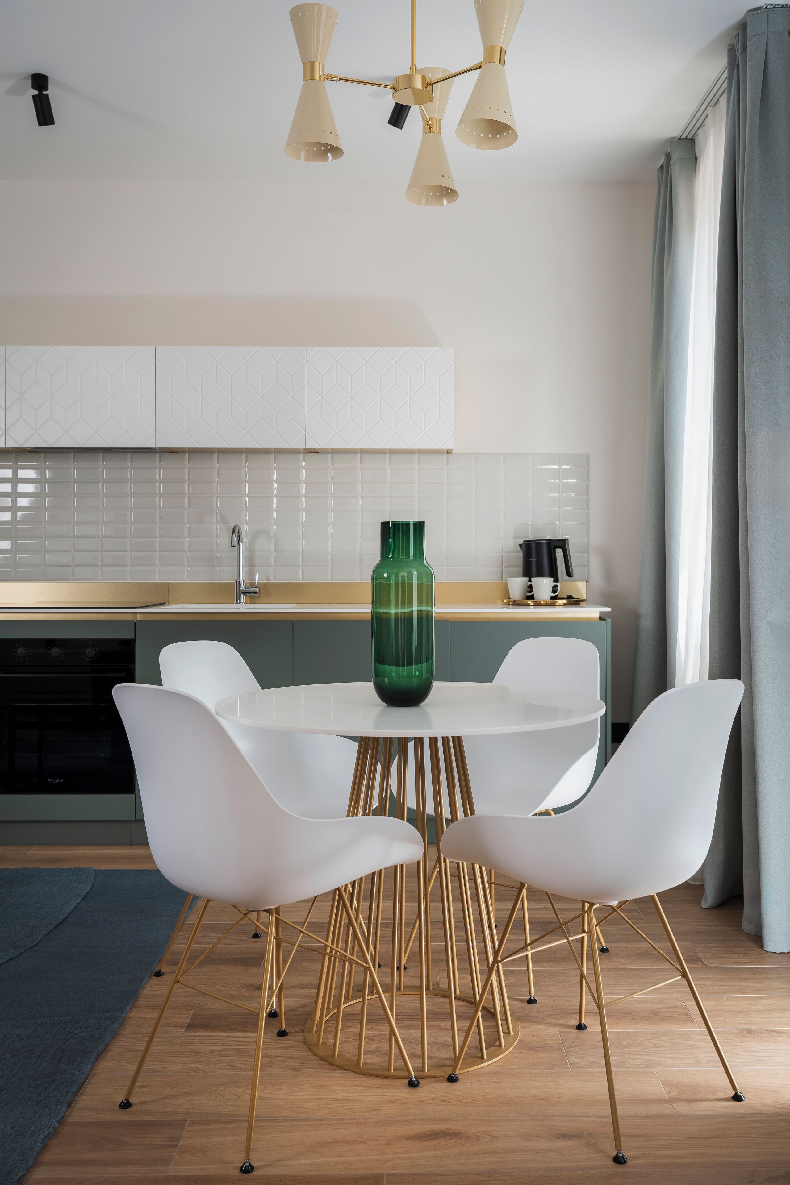 Een moderne keuken met witte kasten, een ronde eettafel met witte stoelen, en een groene vaas.