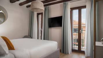 A bedroom with a large bed, a TV mounted on the wall, and a balcony with a view.