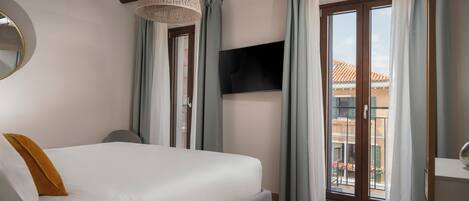 A bedroom with a large bed, a TV mounted on the wall, and a balcony with a view.