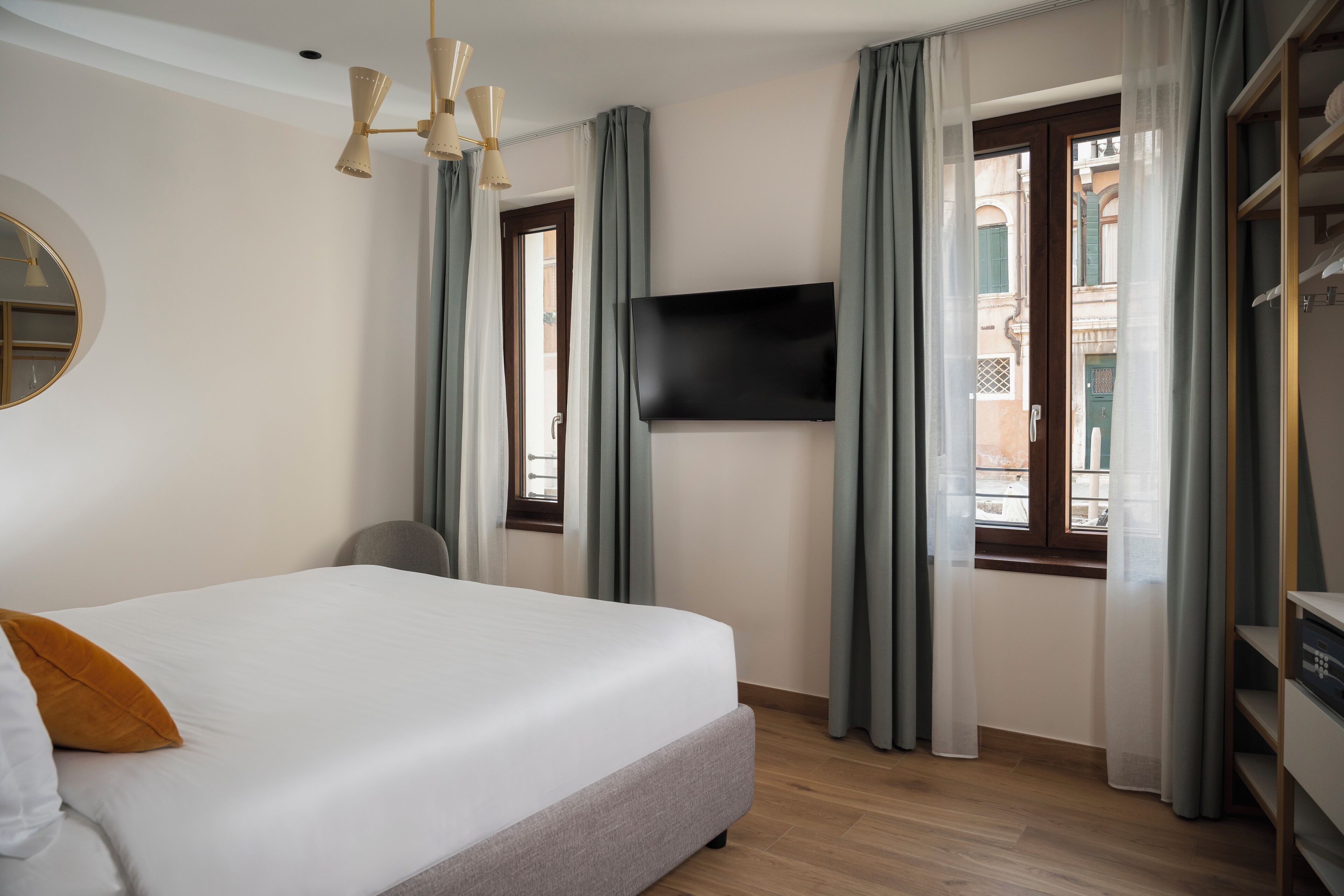 A hotel room with a bed, a TV mounted on the wall, a window with curtains, and a wardrobe.