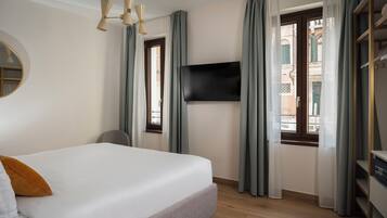 Ein Hotelzimmer mit Bett, Wandfernseher, Fenster mit Vorhängen und Kleiderschrank.