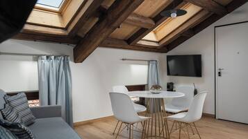 Un dormitorio tipo loft moderno con tragaluces, una zona de comedor con sillas blancas y un televisor de pantalla plana.