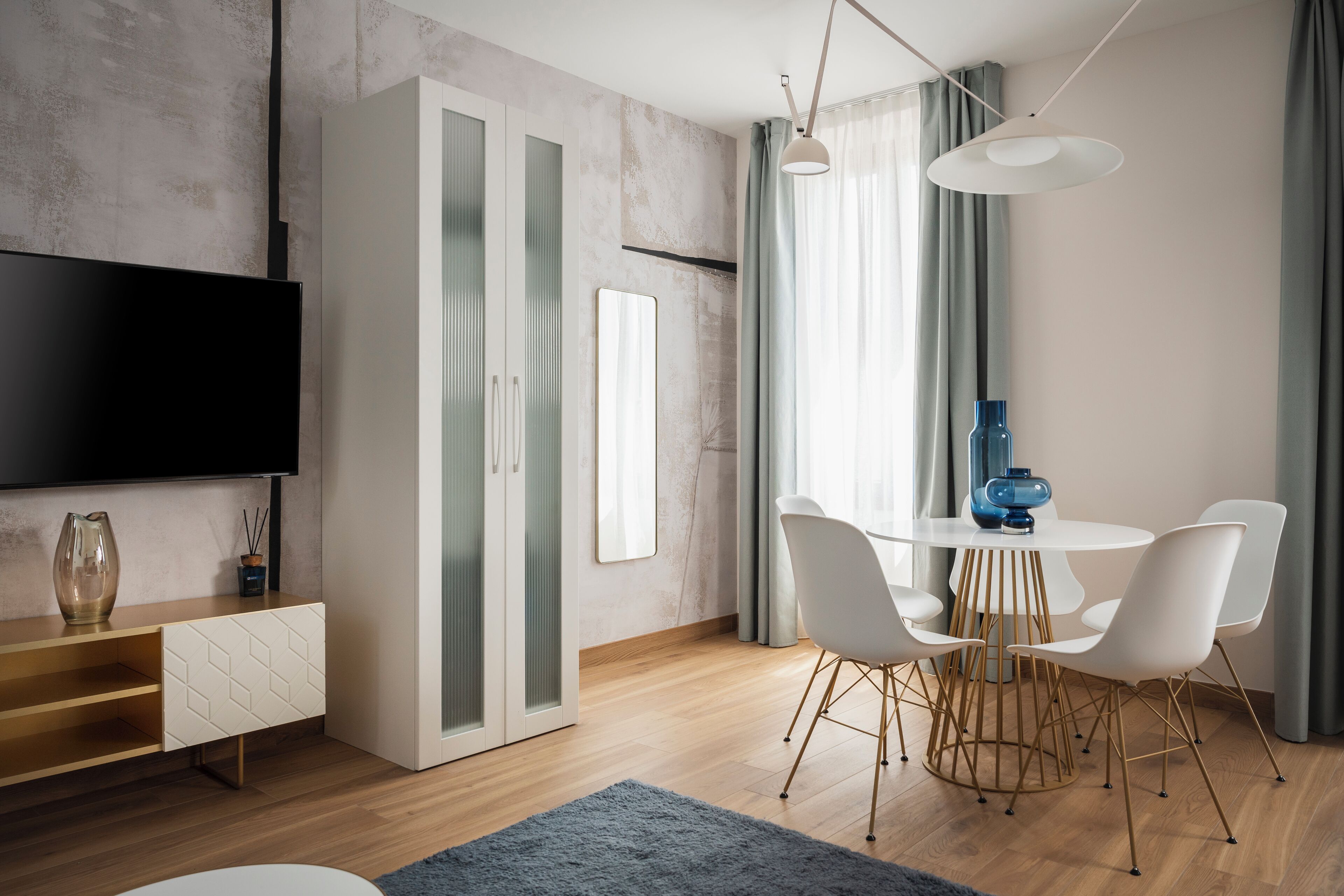 Een moderne woonkamer met een flatscreen televisie, een eettafel met witte stoelen en een blauwe vaas op de tafel.