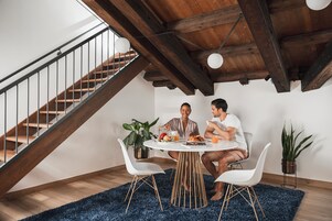 Zona pranzo con scala in legno, sedie bianche, tavolo rotondo e piante in vaso.
