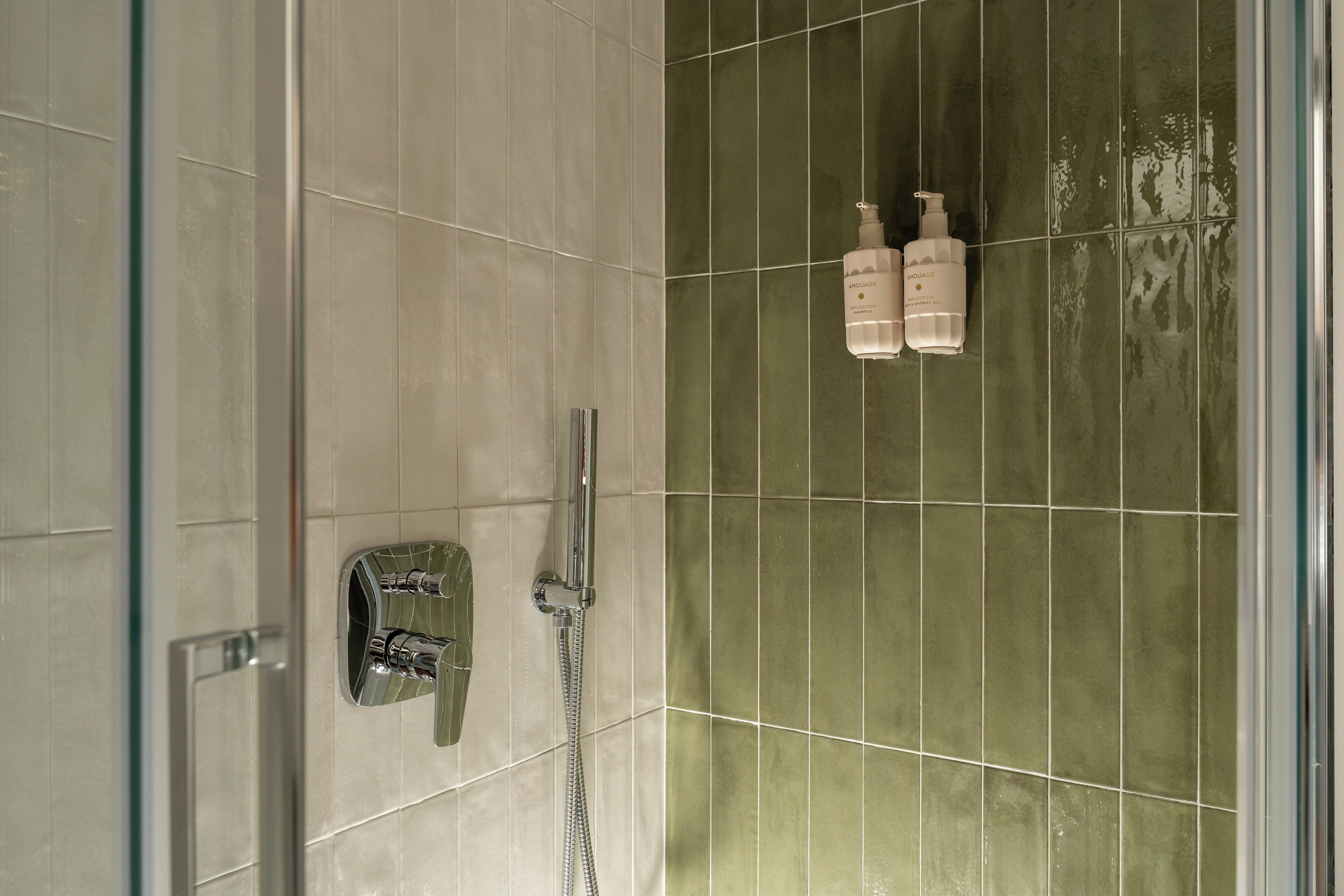 Ein Badezimmer mit Dusche, einer Glastür und zwei Flaschen Amouage Shampoo und Duschgel.