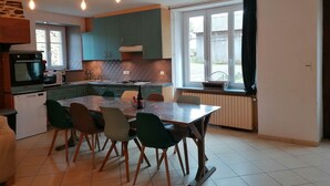 A modern kitchen with teal cabinets, a dining table with chairs, and a large window with curtains. - FALE TAHI - Les Petites rives de la Motte (PLEUGUENEUC)