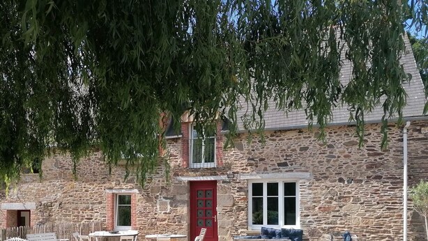 A stone building with a red door, outdoor seating, and a grassy area. - FALE TAHI - Les Petites rives de la Motte (PLEUGUENEUC)