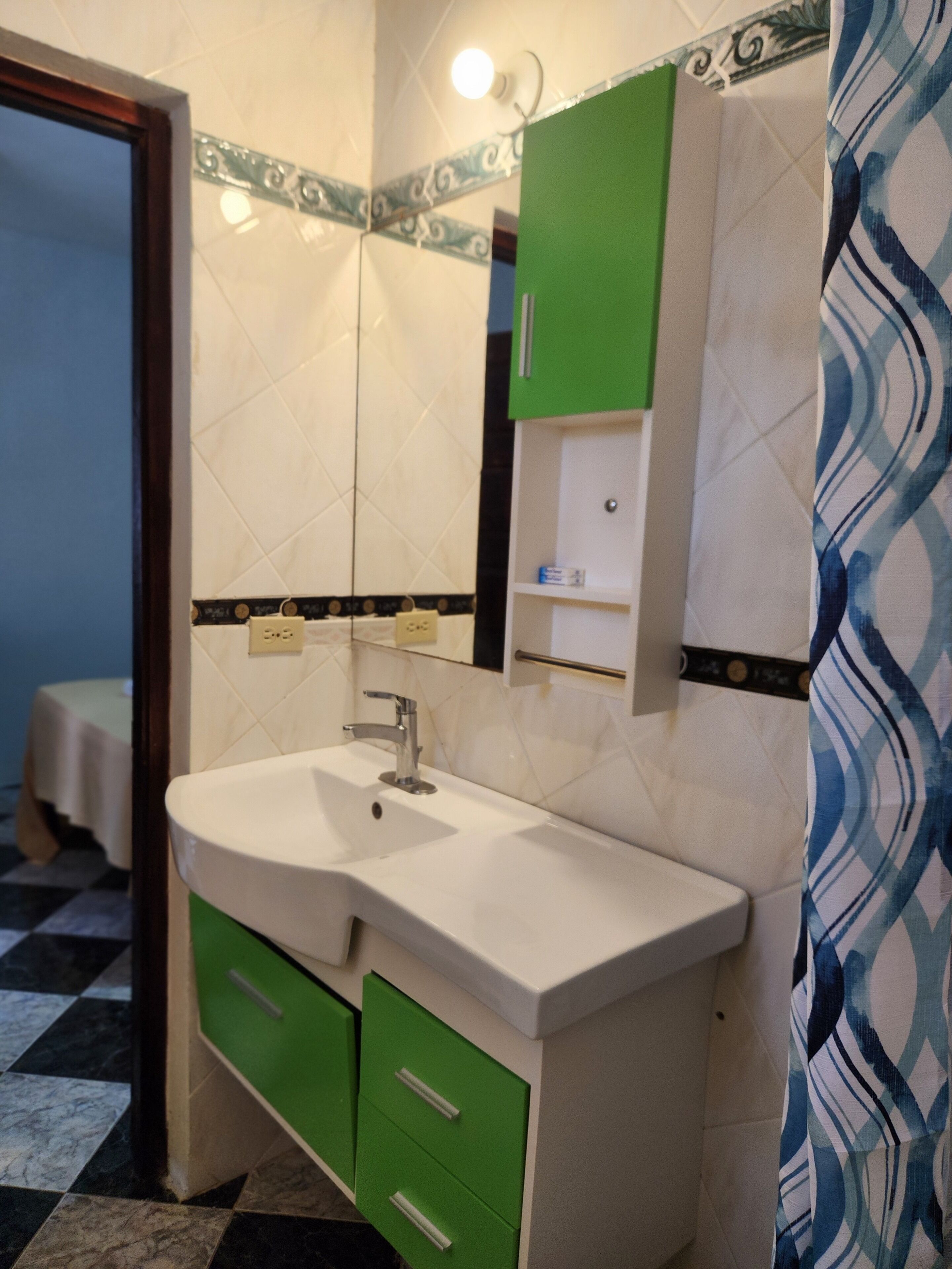 A bathroom with a white sink, green cabinets, and a mirror.