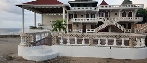A large building with a covered outdoor area, a staircase, and a view of the sea.