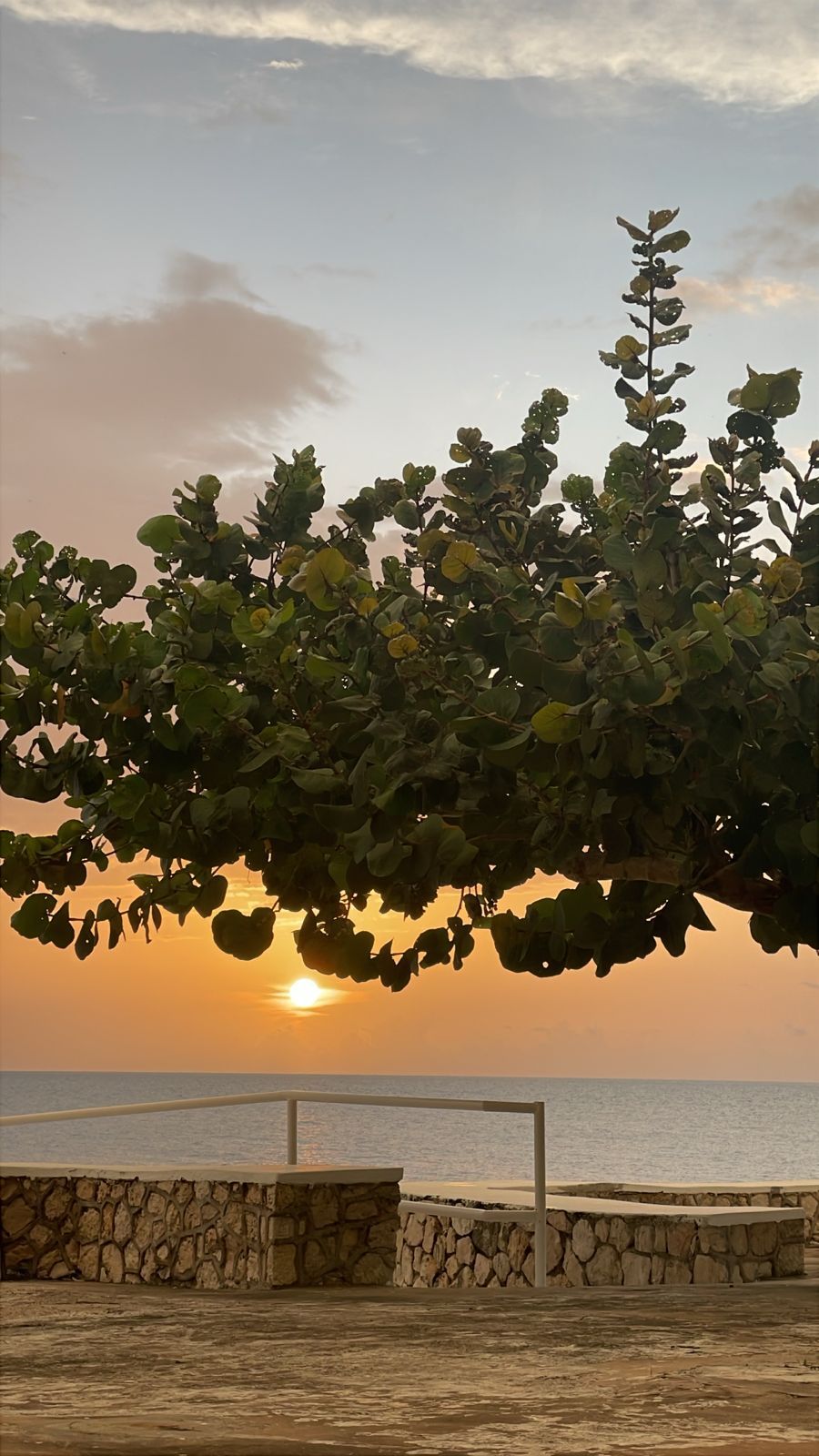 A sunset view with a stone wall and a metal railing in the foreground.