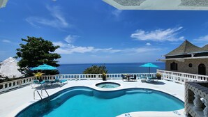 Ein Poolbereich mit Blick auf den Ozean, Liegestühle und Sonnenschirme.