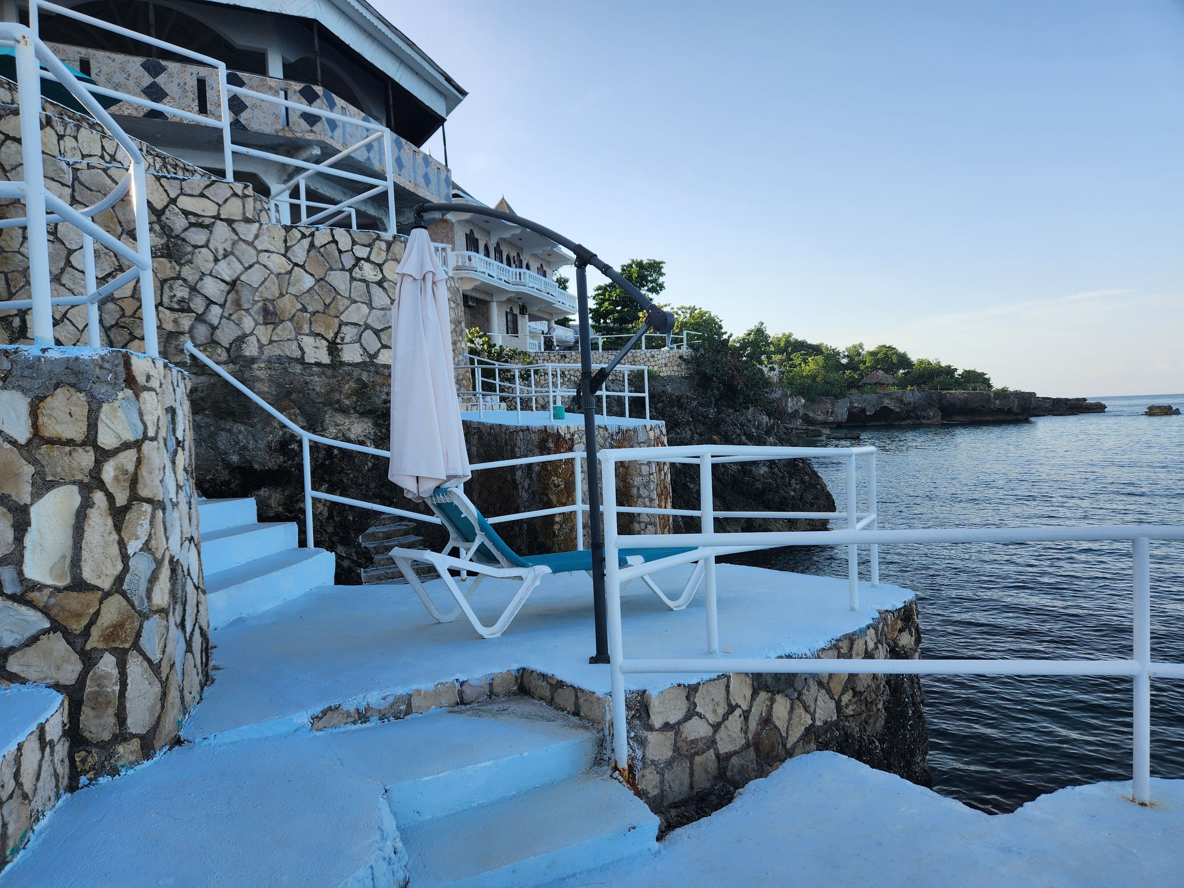A stone staircase leading to a balcony with a white railing, overlooking a body of water.