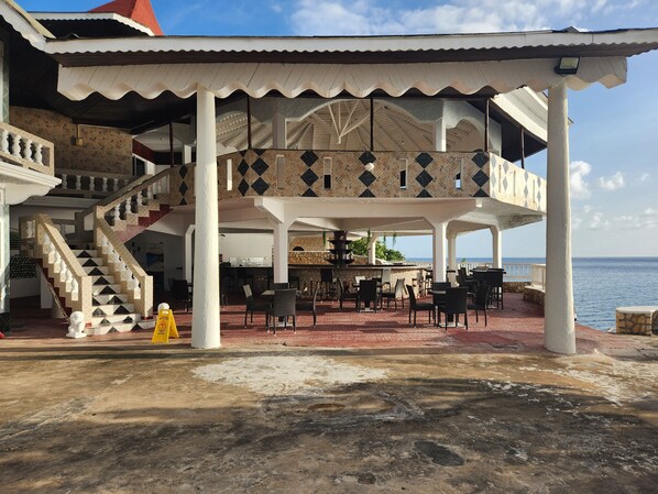 Un espace extérieur abrité, aménagé avec une table à manger, un escalier et offrant une vue sur la mer.