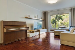 Un soggiorno con un pianoforte, una televisione a schermo piatto, un divano e un'ampia finestra vista verde.