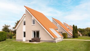 A modern house with a sloped roof, a front porch with outdoor furniture, and a well-maintained lawn. - Summio Zeeland Village (Scharendijke)