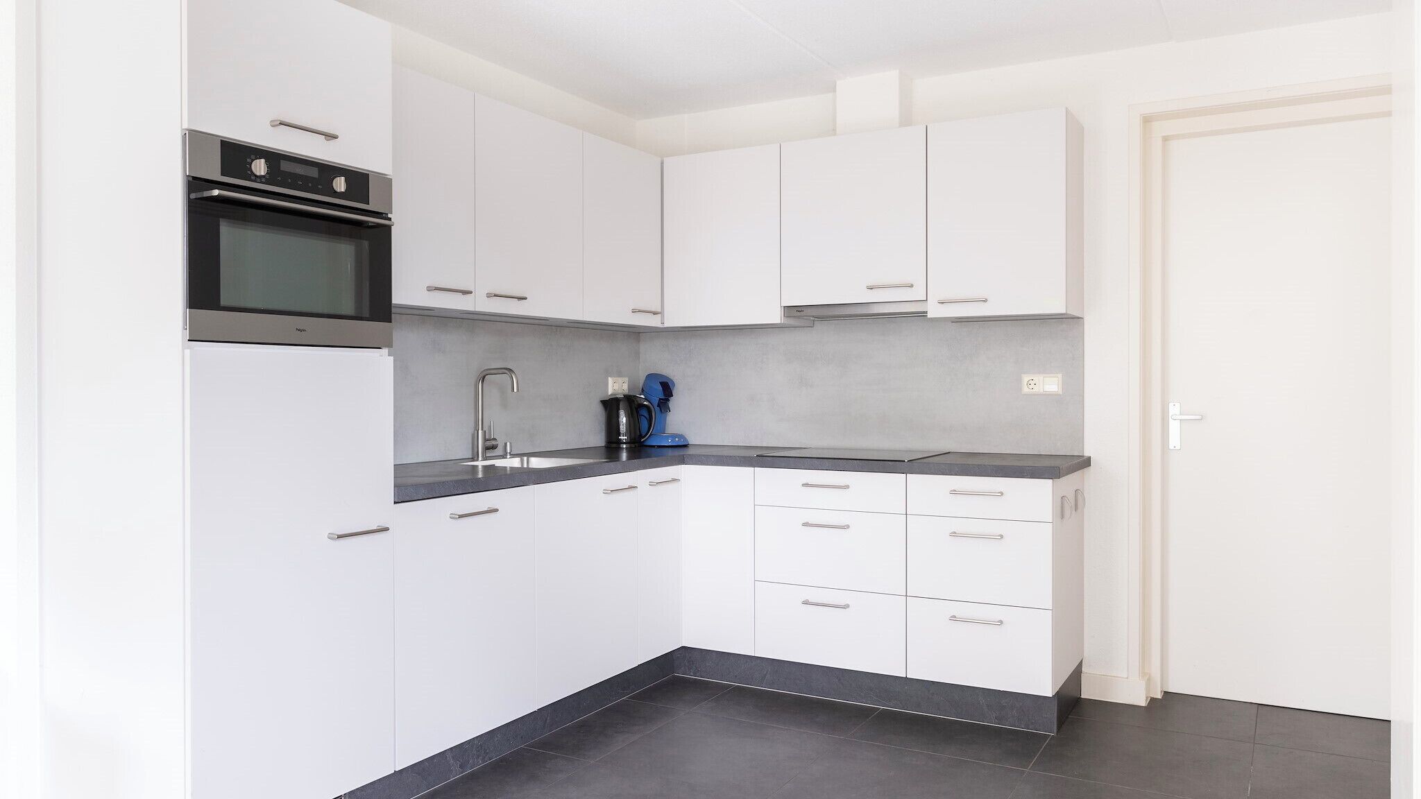 Una cucina moderna con mobili bianchi, forno integrato, lavello e macchina da caffè.