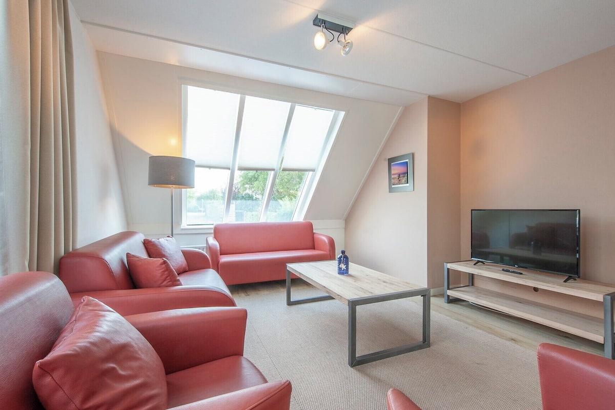 Un salon moderne avec un canapé rouge, un téléviseur à écran plat posé sur un meuble en bois et une grande fenêtre laissant entrer la lumière naturelle.