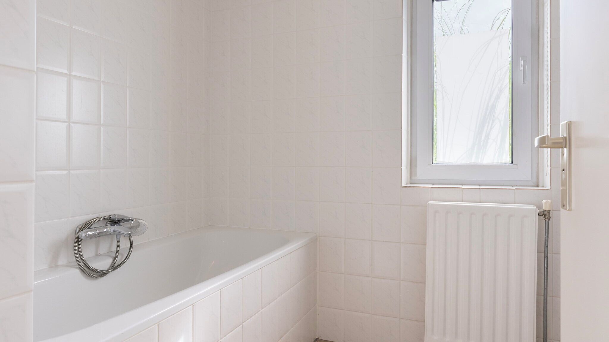 A bathroom with a white bathtub, a window, and a radiator.
