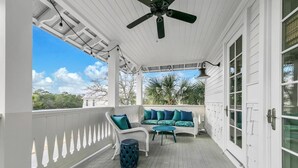 A covered porch with a white railing, a ceiling fan, a wicker sofa with teal cushions, and a small round table. - Cypress by the Sea (Santa Rosa Beach)