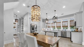 A modern kitchen with white cabinetry, a wooden dining table, and pendant lights. - Cypress by the Sea (Santa Rosa Beach)