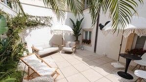 A sunlit patio with a white sofa, two lounge chairs, a small table, and a potted plant.