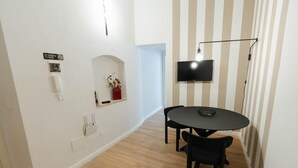A modern dining area with a round table and two chairs, a wall-mounted TV, a no-smoking sign, a Wi-Fi sign, and a small shelf with decorative items.
