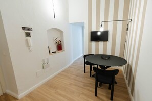 Un comedor moderno con una mesa redonda y dos sillas, un televisor montado en la pared, un letrero de no fumar, un letrero de Wi-Fi y un estante pequeño con adornos.