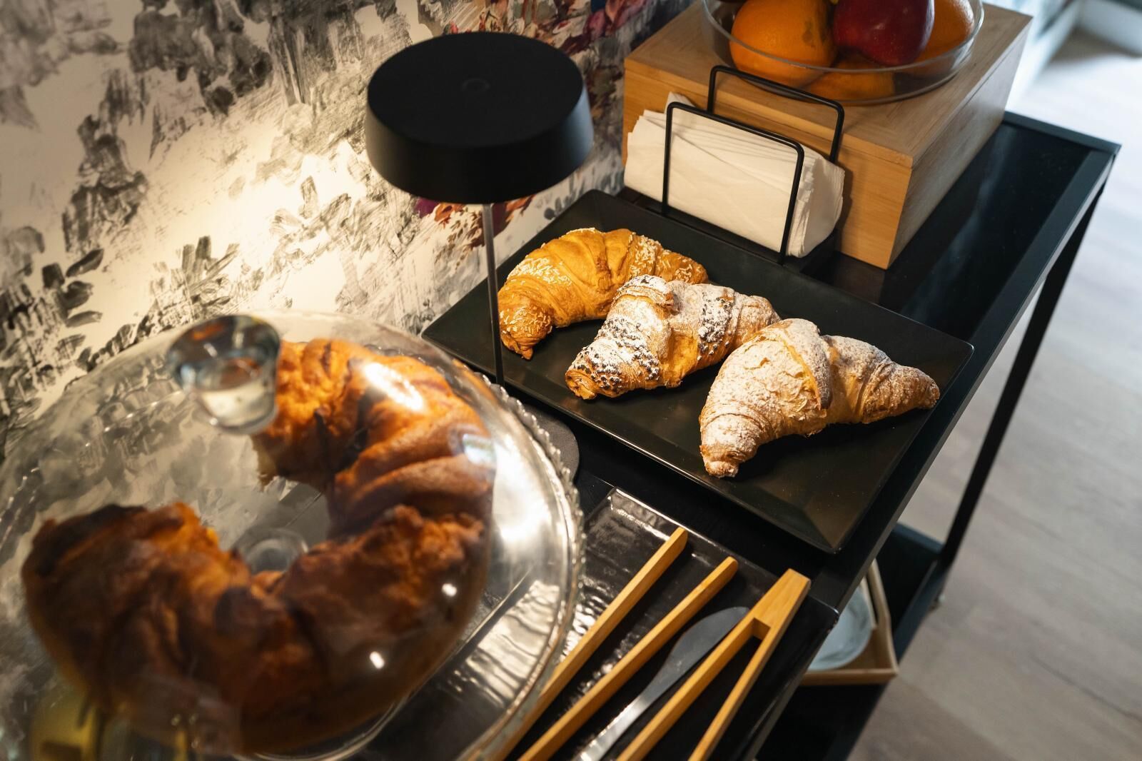 A display of pastries, including a covered pastry dish and a tray with croissants.