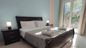 A neatly made bed with a patterned bedspread, two bedside tables with lamps, and a view of the outdoors through a glass door.