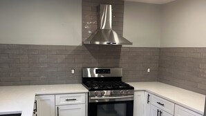 Een moderne keuken met een roestvrijstalen afzuigkap, een inbouwoven en witte kasten.