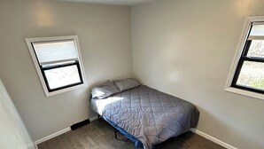 A small, single-bed room with a wooden floor, two windows with blinds, and a ceiling light fixture. - Newly Renovated 4-Bedroom Saugerties Home 10 minutes from HITS with AC and Wi-Fi (Saugerties)