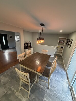 Un comedor con una mesa y sillas de madera, una lámpara colgante y una cocina al fondo.
