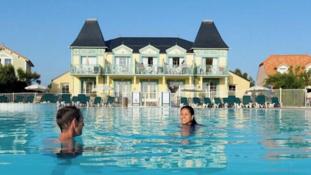 A swimming pool with two people in it, a building with balconies in the background.