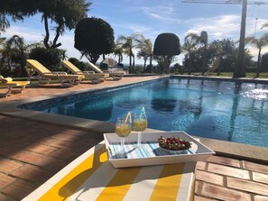 A poolside area with lounge chairs, a table with a tray of fruit and drinks, and a clear view of the pool. - Idyllic Farm House Amazing Landscap Sea View (Loulé)