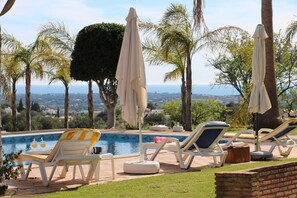 A poolside area with lounge chairs and umbrellas, surrounded by palm trees and a view of the landscape. - Idyllic Farm House Amazing Landscap Sea View (Loulé)