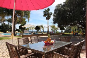A patio area with wicker furniture, a table with a fruit basket, and a red umbrella. - Idyllic Farm House Amazing Landscap Sea View (Loulé)
