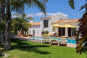 A pool area with lounge chairs and umbrellas, surrounded by a well-maintained lawn and palm trees. - Idyllic Farm House With Huge Garden for 14pax (Loulé)