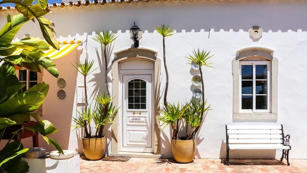 A white building with a tiled patio, a white door, and a bench.