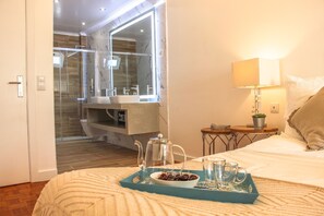 A hotel room with a bed, a bedside table with a lamp, a small table with a plant, and a bathroom visible through an open door. - Luxury Flat With Amazing Terrace in Faro (Faro)