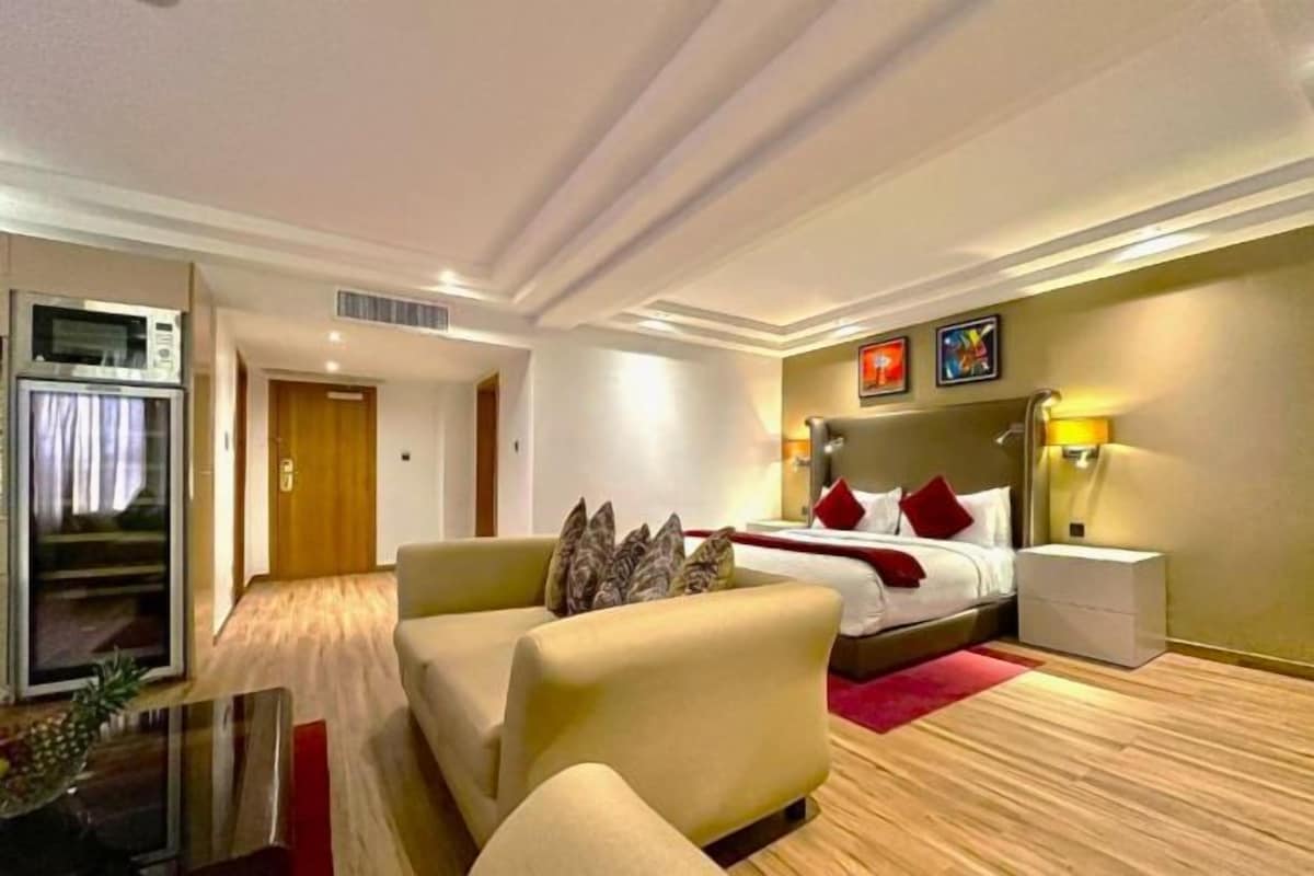 A hotel room with a bed, a sofa, a table, and a refrigerator.