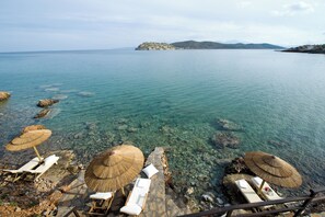 A clear view of a beach with lounge chairs and thatched umbrellas, a rocky shoreline, and a distant island.