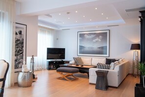 Een moderne woonkamer met een bank, een salontafel en een televisie. Er hangt een groot schilderij aan de muur en staat een potplant.