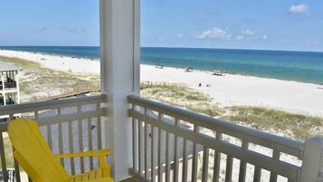 A beach view from a balcony with a yellow chair and a railing.