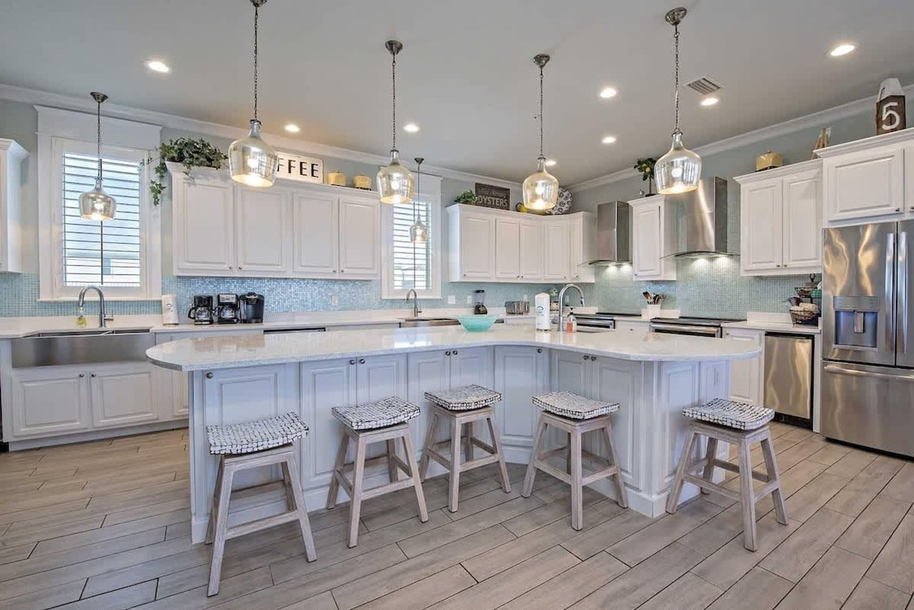 A modern kitchen with white cabinets, a large island with bar stools, pendant lighting, and stainless steel appliances.