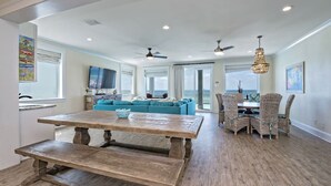 A spacious living area with a wooden dining table, blue sofa, wicker chairs, and a view of the ocean. - Beachfront 18bed Pool Easybreezy (Gulf Shores)