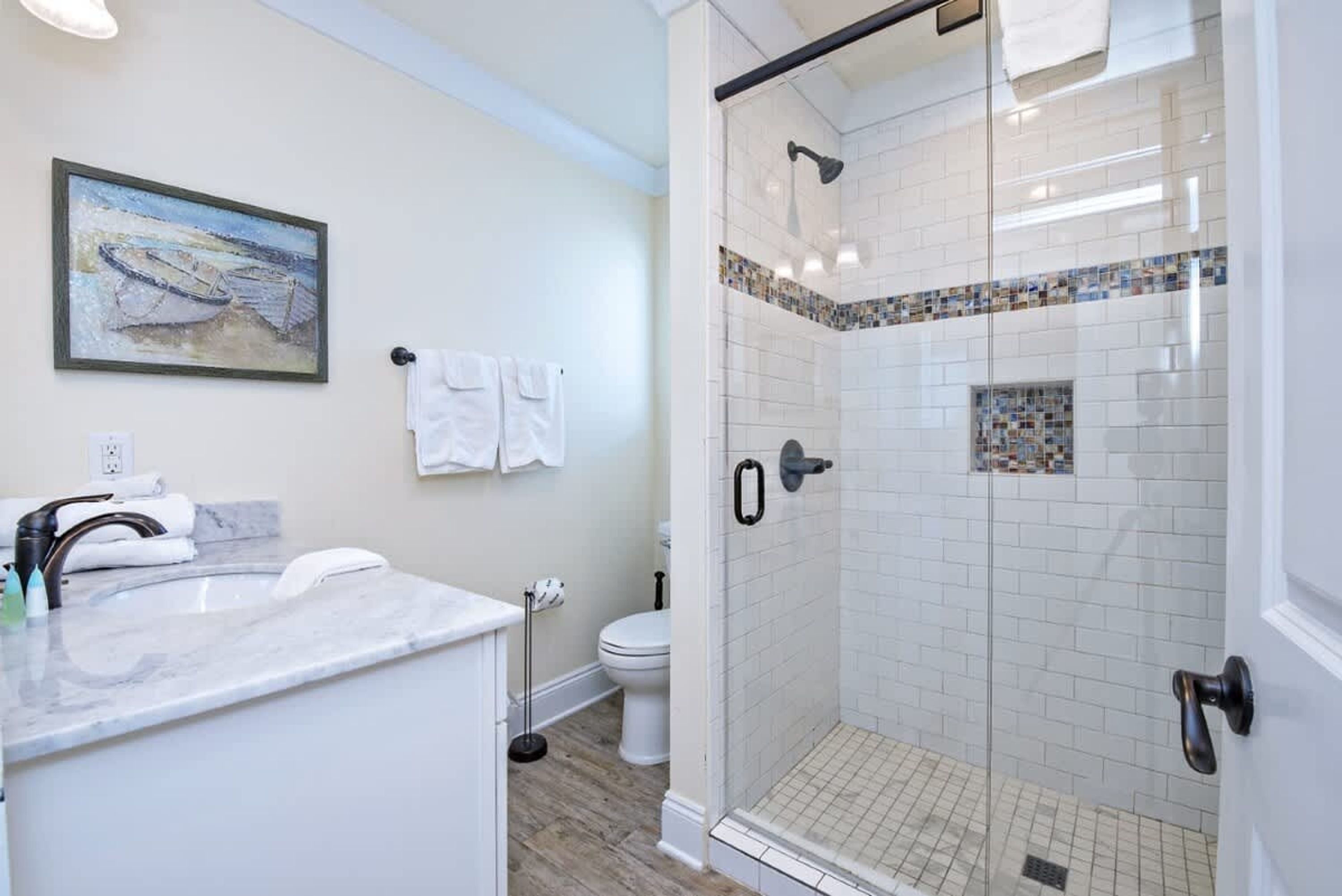 A modern bathroom with a glass-enclosed shower, a marble sink, and a toilet.