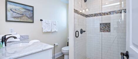 A modern bathroom with a glass-enclosed shower, a marble sink, and a toilet.