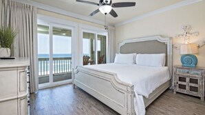 A bedroom with a large bed, a ceiling fan, a nightstand, a lamp, and a view of the ocean through a sliding door. - Beachfront 18bed Pool Easybreezy (Gulf Shores)