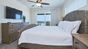 A bedroom with a bed, a ceiling fan, a TV, a dresser, and a view of the ocean.